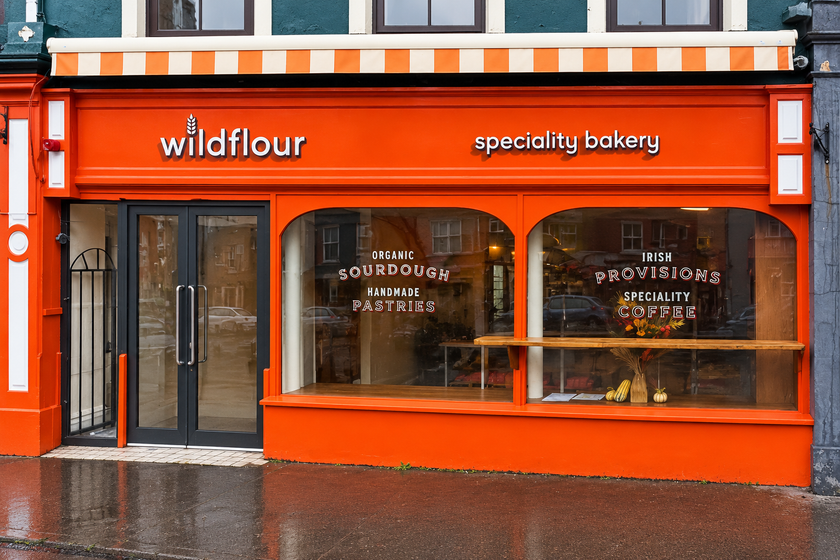 The Wildflour shopfront on New Street, Bantry: a bright orange frontage under a striped awning, with organic sourdough, handmade pastries, Irish provisions and speciality coffee lettered on the windows.