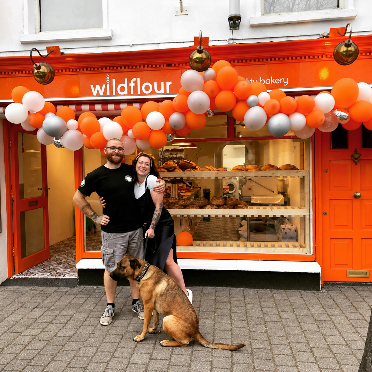 Opening day at Wildflour, Innishannon: the team and their dog outside the orange shopfront under a garland of orange and white balloons.