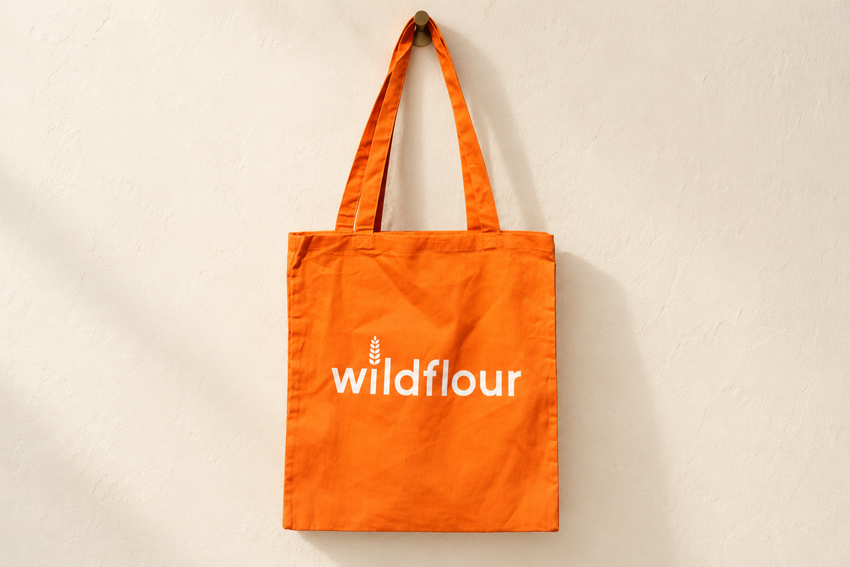 The orange Wildflour tote bag hanging against an ivory wall.