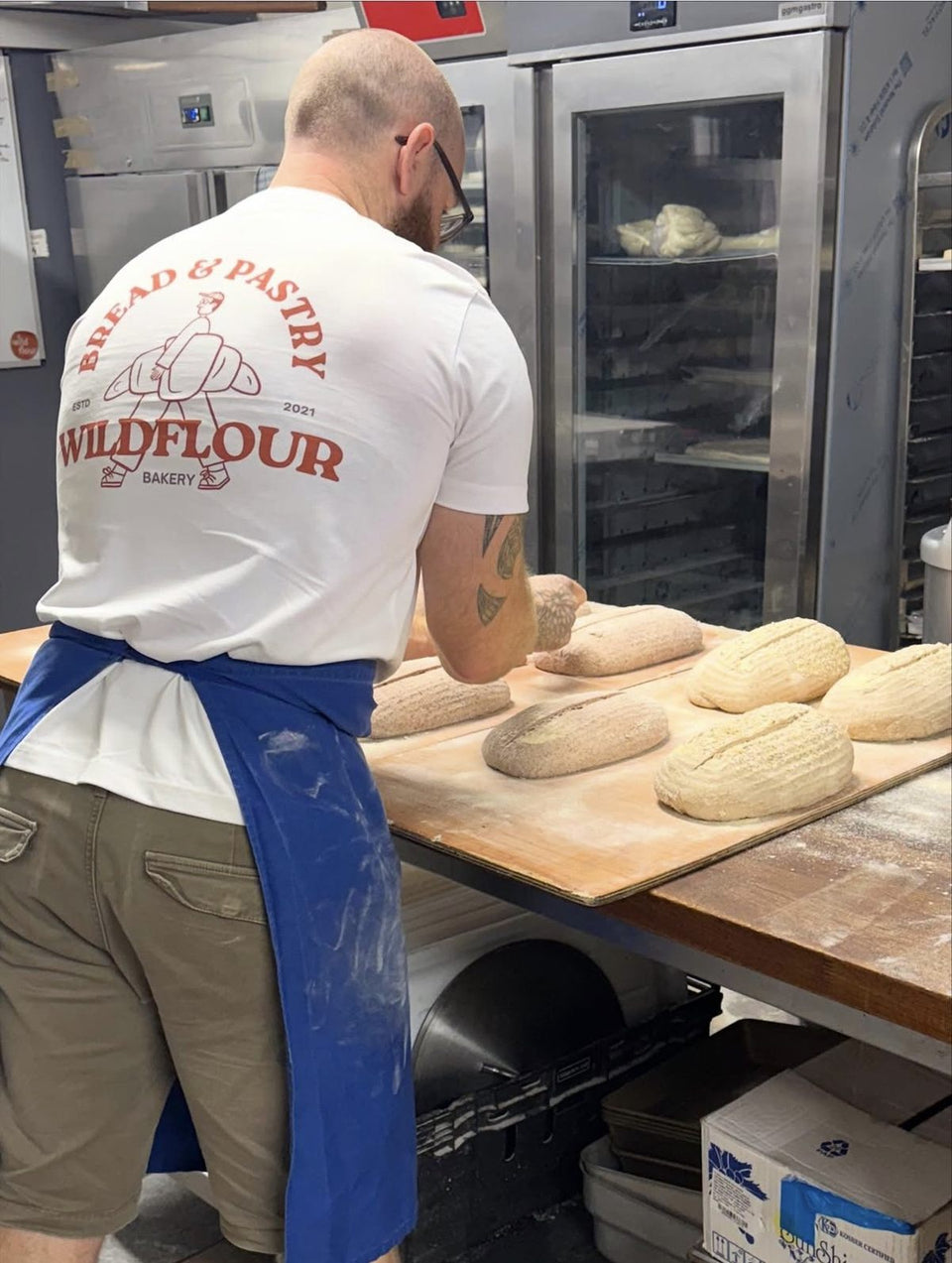 A Wildflour baker shaping sourdough loaves at the bench.