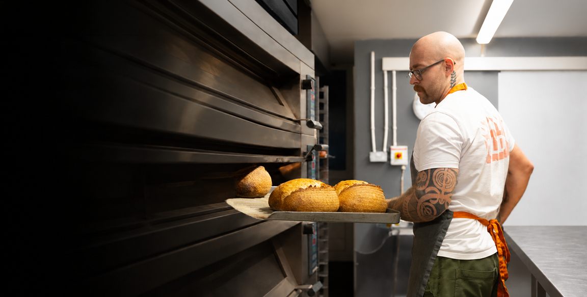 A Wildflour baker drawing a tray of sourdough loaves from the deck oven in the bakery.