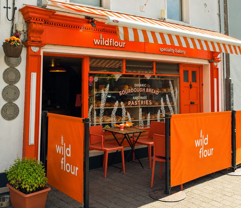 The Wildflour shopfront on Main Street, Innishannon: a bright orange frontage under a striped awning, with "organic sourdough bread" and "hand made pastries" lettered on the window and orange seating outside.